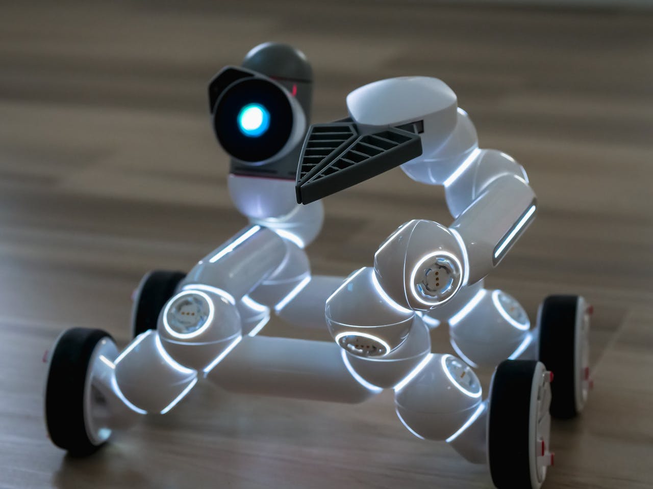who-we-are Close-up of a wheeled robot toy with LED lights on a wooden floor indoors.